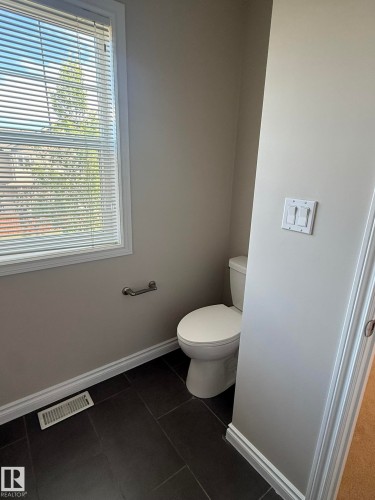 Bathroom featuring dark rectangular floor tiles, a window with horizontal blinds, a white toilet, and light gray painted walls - 8305 Ellis Crescent Nw, Edmonton, AB 