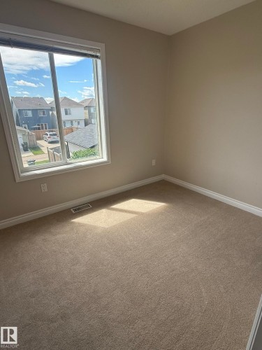 Carpeted room with a large window, neutral wall paint, and white trim - 8305 Ellis Crescent Nw, Edmonton, AB 