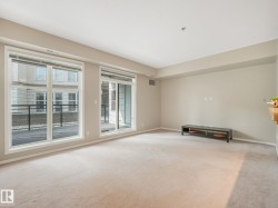 Spacious living area featuring light-colored carpeting, neutral painted walls, and ample natural light from large windows - 