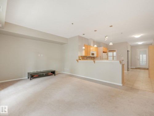 Open-concept living space featuring neutral carpet, recessed lighting, a breakfast bar, light wood-finish cabinetry, and a white refrigerator - 150 4827 104A Street, Edmonton, AB 