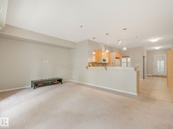 Open-concept living space featuring neutral carpet, recessed lighting, a breakfast bar, light wood-finish cabinetry, and a white refrigerator - 