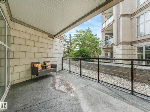 Covered patio featuring a concrete floor, light-colored brick siding, and a black metal and glass railing - 150 4827 104A Street, Edmonton, AB 