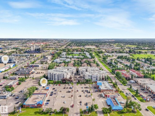 Aerial perspective showcasing a mixed-use urban landscape featuring commercial structures, multi-story residential buildings, and extensive paved parking areas - 150 4827 104A Street, Edmonton, AB 