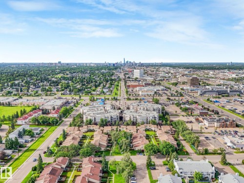 Aerial perspective showcasing a residential area with varied housing types, extensive green spaces, and a distant city skyline - 150 4827 104A Street, Edmonton, AB 