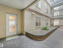 Ground-level entry featuring a frosted glass door, textured stucco facade, and a decorative concrete pathway - 150 4827 104A Street, Edmonton, AB 