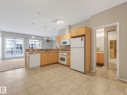 Open-concept kitchen featuring light wood cabinetry, a built-in microwave, integrated dishwasher, and tile flooring - 150 4827 104A Street, Edmonton, AB 