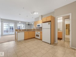 Open-concept kitchen featuring light wood cabinetry, a built-in microwave, integrated dishwasher, and tile flooring - 