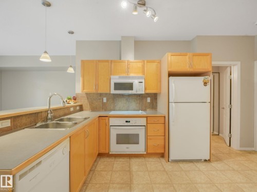 Kitchen featuring light wood cabinetry, white built-in oven, white microwave, white refrigerator, and tiled flooring - 150 4827 104A Street, Edmonton, AB 