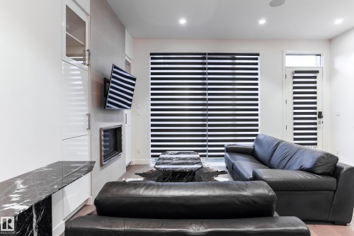 Living area featuring a sleek linear fireplace, built-in cabinetry with a black marble-look countertop, recessed lighting, and wood-finish flooring - 13218 102 Avenue, Edmonton, AB 