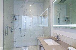 Modern bathroom featuring a frameless glass shower enclosure with white marbled tile surround and built-in shelving - 