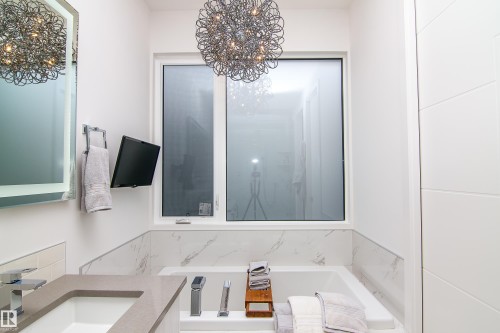 Modern bathroom featuring a built-in tub with marble-look surround, large window, and contemporary vanity with integrated sink - 13218 102 Avenue, Edmonton, AB 