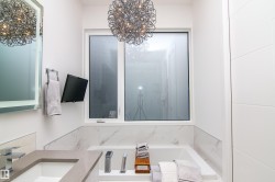 Modern bathroom featuring a built-in tub with marble-look surround, large window, and contemporary vanity with integrated sink - 