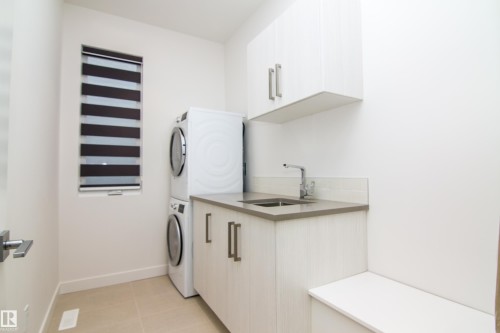 Laundry area featuring a stacked washer and dryer, light wood-finish cabinetry, a sink with a chrome faucet, and a light-colored countertop - 13218 102 Avenue, Edmonton, AB 