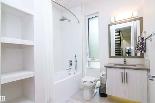 Contemporary bathroom featuring a white tile shower with tub, a wood-finish vanity with a rectangular sink and stone-finish countertop, and a framed mirror with integrated lighting - 13218 102 Avenue, Edmonton, AB 