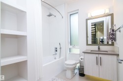 Contemporary bathroom featuring a white tile shower with tub, a wood-finish vanity with a rectangular sink and stone-finish countertop, and a framed mirror with integrated lighting - 