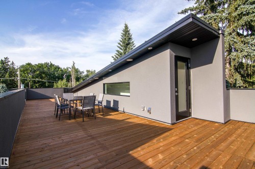 Expansive rooftop deck featuring wood flooring, a contemporary grey stucco exterior, a black framed entry door, and a horizontal window - 13218 102 Avenue, Edmonton, AB 