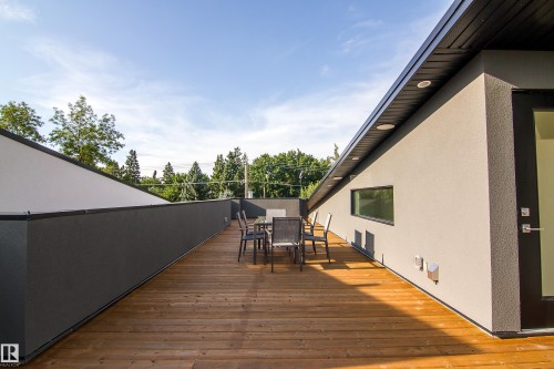 Expansive outdoor terrace featuring wood-finish decking, a low-profile perimeter wall, stucco exterior, and a black-framed glass door - 13218 102 Avenue, Edmonton, AB 