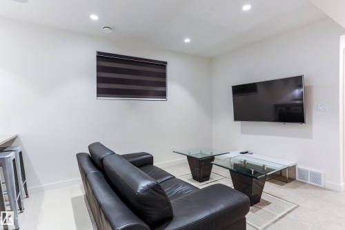 Recessed ceiling lighting illuminates a room with a wall-mounted television, a window with a banded roller shade, and light-toned flooring - 13218 102 Avenue, Edmonton, AB 