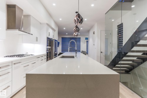 Open-concept kitchen featuring a waterfall island, integrated stainless steel appliances, and sleek white cabinetry - 13218 102 Avenue, Edmonton, AB 