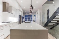 Open-concept kitchen featuring a waterfall island, integrated stainless steel appliances, and sleek white cabinetry - 