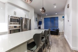 Modern kitchen featuring a large island with seating, stainless steel appliances, white high-gloss cabinetry, recessed lighting, and wood-finish flooring - 
