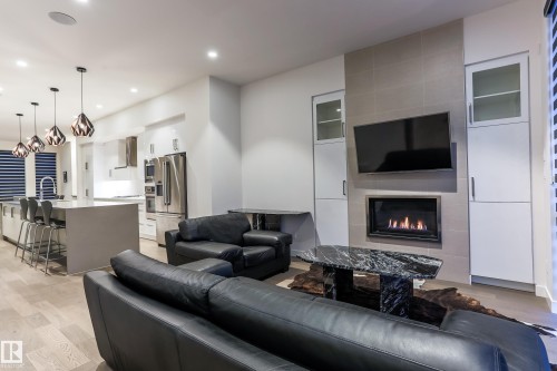 Open-concept living area featuring a kitchen island with pendant lighting, wood-finish flooring, a built-in fireplace with a tiled surround, and integrated cabinetry - 13218 102 Avenue, Edmonton, AB 