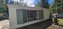 White horizontal siding exterior with a dark green trimmed window and shutters, featuring a partially visible wood deck, and a decorative brick well structure - 