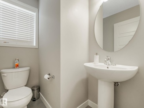 Pedestal sink with chrome faucet, oval mirror, and white toilet - 55 4470 Prowse Road, Edmonton, AB 