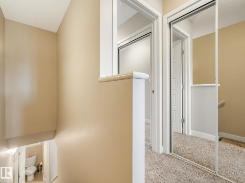 Hallway with mirrored closet doors, neutral carpet, and beige wall paint - 55 4470 Prowse Road, Edmonton, AB 