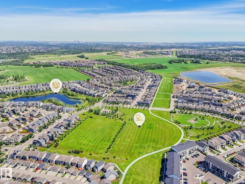 Aerial perspective showcasing a residential community with abundant green spaces, multiple residential structures, two distinct bodies of water, and surrounding undeveloped land - 55 4470 Prowse Road, Edmonton, AB 