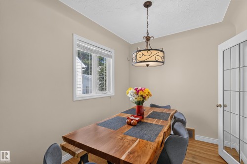 Dining area featuring hardwood flooring, a decorative ceiling light fixture, a window with white blinds, and a white French door - 11015 122 Street, Edmonton, AB 