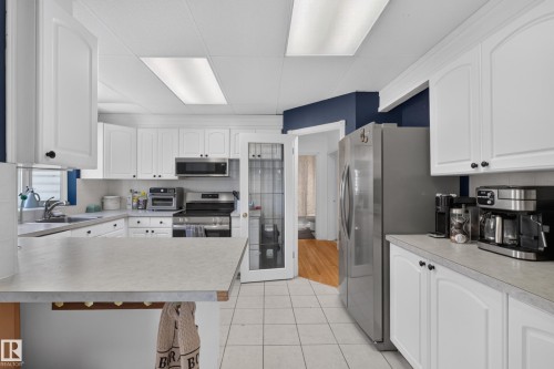 Kitchen featuring white cabinetry, light countertops, stainless steel appliances, and tile flooring - 11015 122 Street, Edmonton, AB 