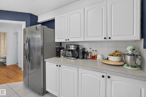 Kitchen featuring white cabinetry with black hardware, a light-toned countertop, a tile backsplash, and a stainless steel refrigerator - 11015 122 Street, Edmonton, AB 