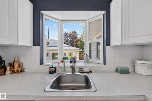 Kitchen with a stainless steel sink, bay window, white cabinetry, and a light-toned countertop - 11015 122 Street, Edmonton, AB 