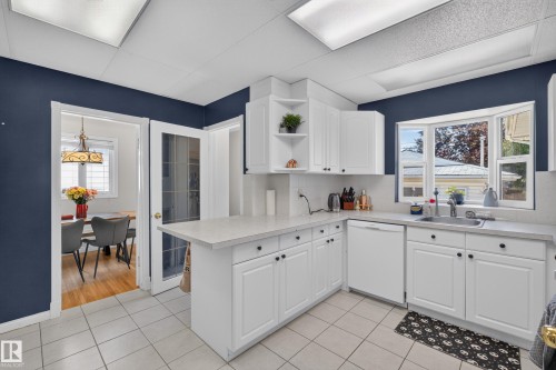 Kitchen featuring white cabinetry, light-toned countertops, a stainless steel sink, a bay window, and tile flooring - 11015 122 Street, Edmonton, AB 