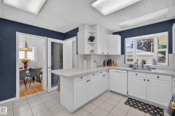 Kitchen featuring white cabinetry, light-toned countertops, a stainless steel sink, a bay window, and tile flooring - 