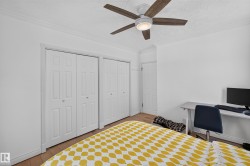 Room featuring wood-finish flooring, two sets of bi-fold closet doors, a ceiling fan with integrated lighting, and crown molding - 