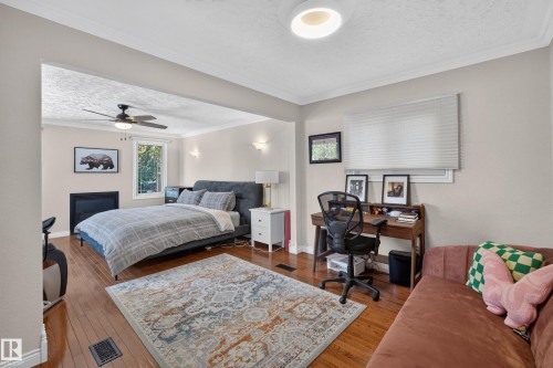 Expansive room featuring hardwood flooring, crown molding, a built-in fireplace, a ceiling fan with integrated lighting, and multiple windows - 11015 122 Street, Edmonton, AB 