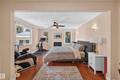 Hardwood-style flooring throughout this room, featuring multiple windows, crown molding, a ceiling fan with integrated lighting, and a built-in fireplace - 11015 122 Street, Edmonton, AB 