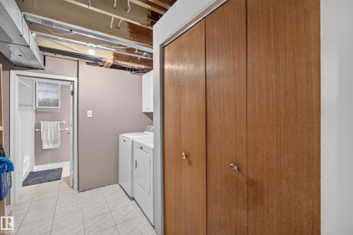 Laundry area featuring a side-by-side washer and dryer, adjacent to a full bathroom with a tiled shower/tub combination and window - 11015 122 Street, Edmonton, AB 
