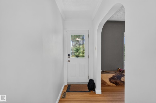 Entryway featuring a white door with decorative glass inserts, wood-finish flooring, and an arched doorway - 11015 122 Street, Edmonton, AB 