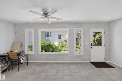 Sunroom featuring light-toned tile flooring, textured wall finish, and a ceiling fan - 