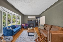 Living space featuring a prominent bay window, a central fireplace with a dark mantel, wood-finish flooring, and a textured ceiling - 