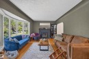 Living space featuring a prominent bay window, a central fireplace with a dark mantel, wood-finish flooring, and a textured ceiling - 11015 122 Street, Edmonton, AB 