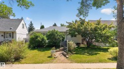 Front exterior featuring a white siding facade, gray shingle roof, and a mature tree - 