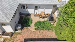 Rear exterior featuring a white siding finish, shingle roofing, and a concrete patio area - 