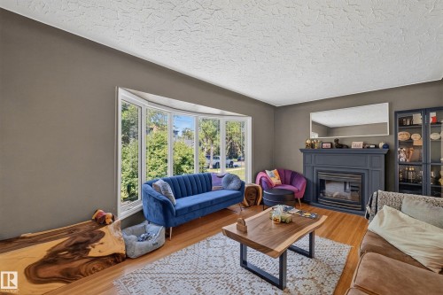 Living area featuring a prominent bay window, hardwood flooring, a fireplace with a decorative mantel, and textured ceilings - 11015 122 Street, Edmonton, AB 