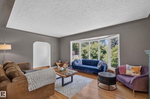 Bright living area with wide bay windows, wood-finish flooring, and a textured ceiling - 11015 122 Street, Edmonton, AB 