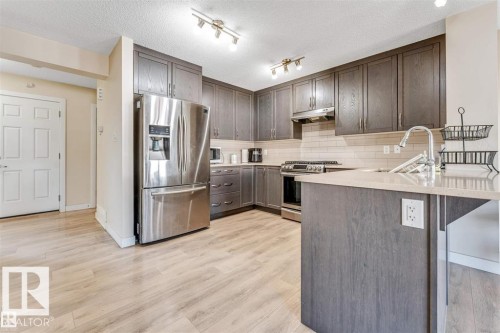Contemporary kitchen featuring wood-finish flooring, dark wood-finish cabinetry, stainless steel appliances, a light-toned countertop, and a subway tile backsplash - 1715 27 Street, Edmonton, AB 