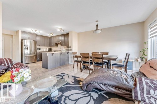 Open-concept living space featuring wood-finish flooring, a kitchen with dark cabinetry and stainless steel appliances, a kitchen island with seating, a dining area with overhead lighting, and a window with blinds - 1715 27 Street, Edmonton, AB 